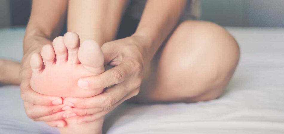 women in bed holding foot due to foot pain